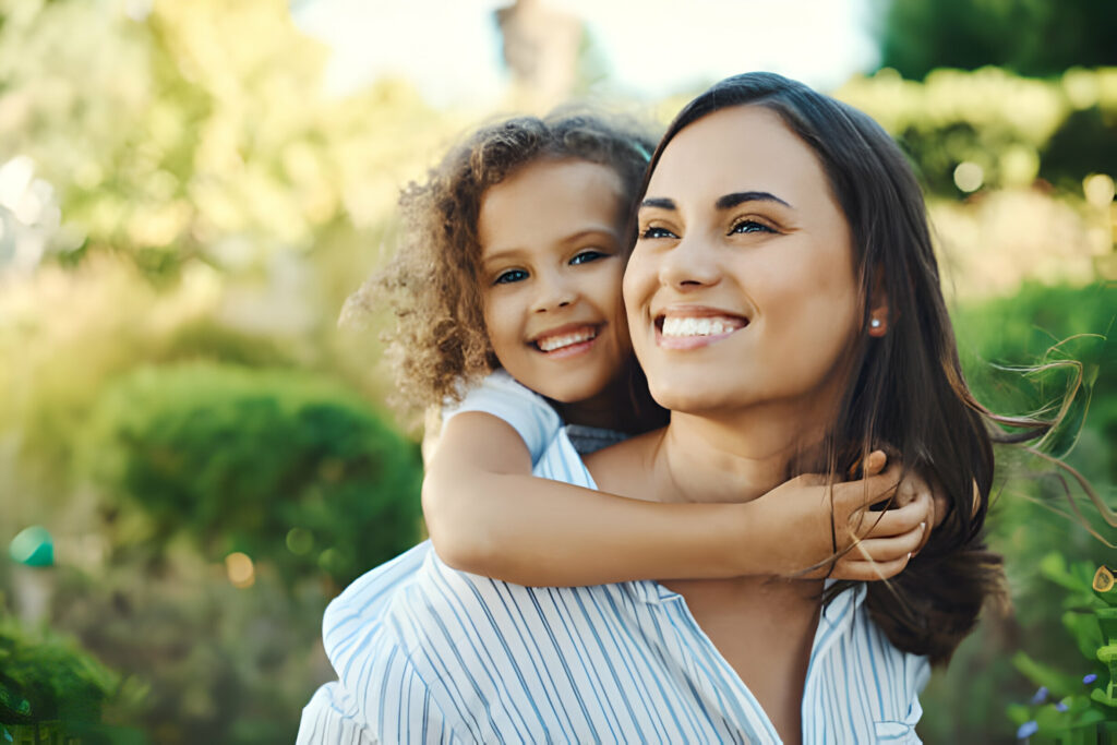 A smiling woman embraces a joyful young girl outdoors.