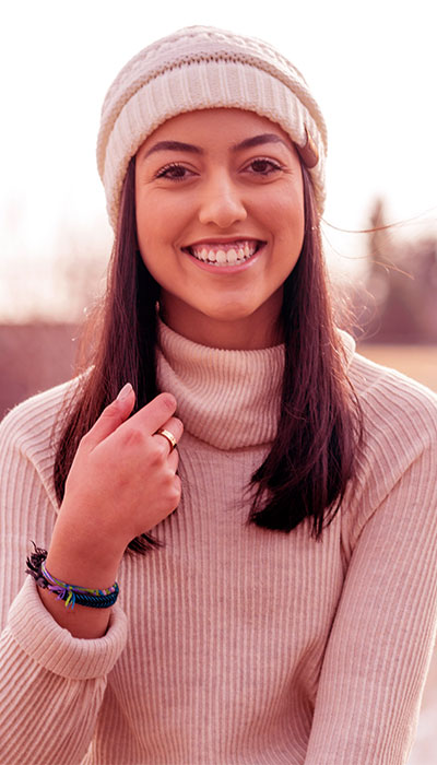 Young woman smiling warmly, wearing a light pink sweater and bracelets.